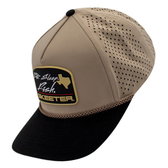 Side of a beige and black cap with perforated mesh back and a black rubber patch on the front. 